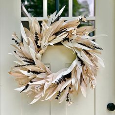 a wreath made out of feathers on a white door with a window in the background