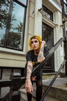 a woman with yellow hair and tattoos on her arm sitting on the steps in front of a building