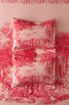 three red and white pillows sitting on top of a bed next to a pink wall