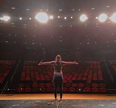 a woman is standing in front of an empty stage with her arms outstretched and hands out