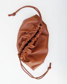 a brown leather purse with ruffles on the front and side, sitting on a white surface