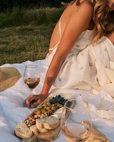 a woman sitting on a blanket with some food and wine in front of her,