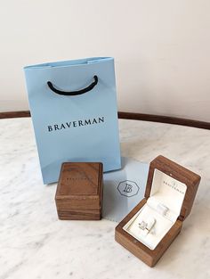 two wooden boxes with rings in them sitting on a marble table next to a paper bag