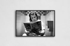 a man reading a book while sitting on a toilet in a bathroom with tiled walls