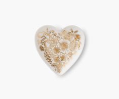 a white and gold heart shaped dish with flowers on the side, against a white background