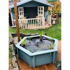 a small pond in the middle of a wooden decked area next to a blue shed