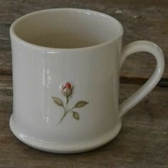 a white coffee cup with a rose painted on the side and bottom, sitting on a wooden table