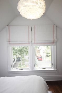 a bedroom with two windows and a white bed in front of the window is lit by a round light fixture