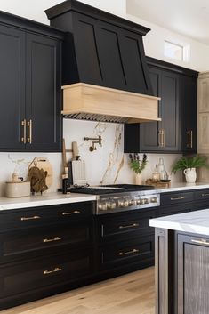 a kitchen with black cabinets and marble counter tops, an oven hood over the stove