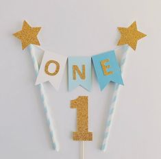 a one year birthday cake topper with gold glitter stars and streamers on it