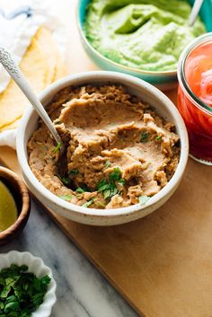 a wooden cutting board topped with bowls filled with hummus and guacamole