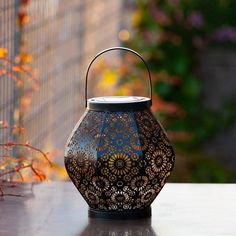 a black lantern sitting on top of a table next to some flowers and plants in the background