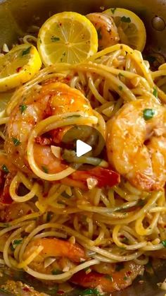 a bowl filled with pasta and shrimp next to lemon wedges