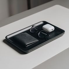 a pair of glasses sitting on top of a black tray next to an earbud