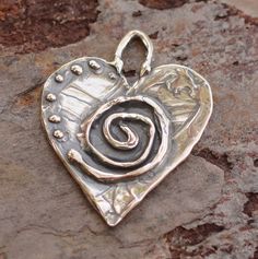 Spiral Adorned Heart!  These are light-weight yet very durable.  The backside is smooth. Carl Jung, the famous psychiatrist, said that the spiral is an archetypal symbol that represents cosmic force.  Some consider the spiral a symbol of the spiritual journey. Also considered to represent the evolutionary process of learning and growing.  The 7 dots are symbolic!  It's the perfect number and symbol of  divine abundance. -Size 20mm x 20mm -Loop is about 5x3mm -Thickness at center is 2mm -Sterling Silver -Option for Jump Ring: 16 gauge sterling silver (5mm inside diameter) You will need a jump ring to hang nicely on a necklace or to attach to a bracelet. If you are knotting on leather for a necklace then you don't need one. The round jump ring is a standard 16 gauge shown in last photo. Plea Sacred Spiral, Pmc Jewelry, Silversmithing Jewelry, Learning And Growing, Mexican Earrings, Ormond Beach, Metal Clay Jewelry, Precious Metal Clay, Beads Online