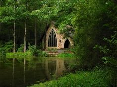 an old church in the middle of a forest next to a lake with trees around it