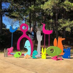 a woman standing next to colorful sculptures in the shape of hands and birds with trees behind her