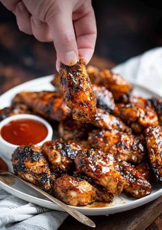 someone is dipping sauce on chicken wings with ketchup in a white plate, ready to be eaten