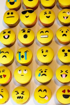 many yellow cupcakes with different emoticions are arranged on a white surface