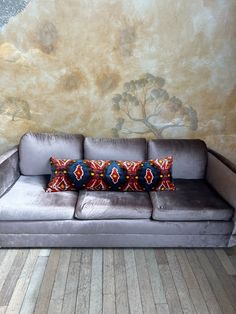 a gray couch sitting on top of a wooden floor next to a wall with a painting