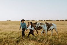 a man walking with two horses in a field