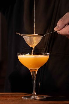 a person pours orange juice into a martini glass with a strainer in it