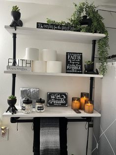 a shelf with candles, plants and other items on it in a white walled room