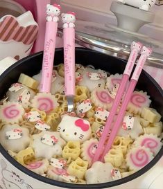 three hello kitty utensils are in a pot with noodles and other food items