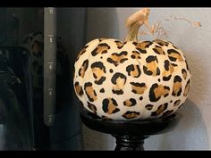 a leopard print pumpkin sitting on top of a black stand next to a white wall