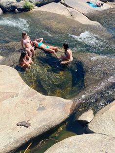 some people are sitting on rocks in the water and one person is laying down next to them