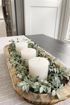 three candles sitting on top of a wooden tray filled with greenery and eucalyptus leaves