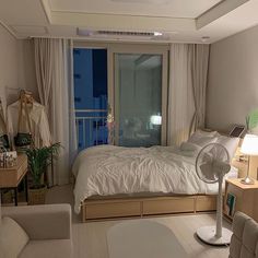 a bedroom with a bed, desk and fan in it's corner area next to a window