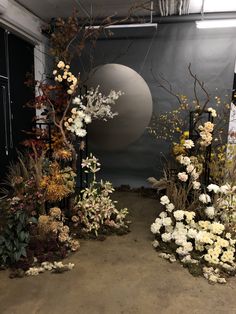 an arrangement of flowers and plants in front of a gray wall with a circular object