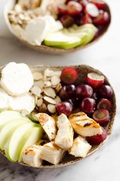 two bowls filled with different types of fruit and cheese on top of a marble counter