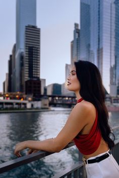 a woman in a red top is standing on a bridge looking at the water and buildings