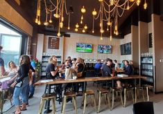 a group of people sitting at tables in a restaurant with lights hanging from the ceiling