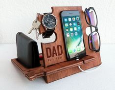 an iphone, watch, and glasses are on a wooden stand with a cell phone in it