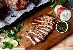 sliced pork on a cutting board with garnishes and condiments next to it