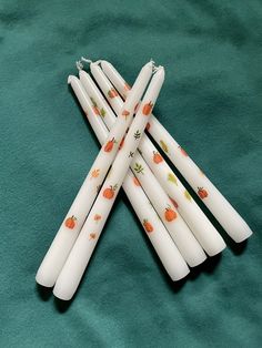 six white candles with pumpkins on them sitting on a green cloth covered tablecloth