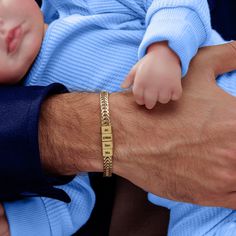 a close up of a person holding a baby wearing a gold bracelet with words on it