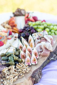 an assortment of fruits and vegetables arranged on a wooden platter with grapes, strawberries, melon, walnuts