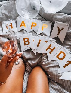 a woman holding a wine glass in her hand with happy birthday signs on the bed