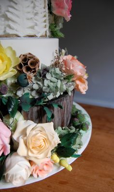 a three tiered wedding cake with flowers on the top and bottom, sitting on a wooden table