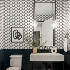 a white toilet sitting under a bathroom mirror next to a sink with a vase on top of it