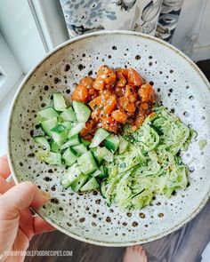 a person holding a bowl filled with cucumbers and meat on top of it