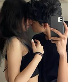 a man and woman kissing in front of a mirror with their cell phones up to their faces