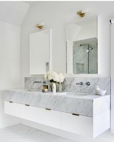 a white bathroom with marble counter tops and double sinks, gold faucets and mirrors