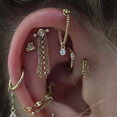 an ear with several different types of piercings attached to it's sides and chains hanging from them