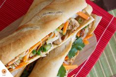 two sandwiches with meat, cheese and veggies are on a red tray next to a green mat