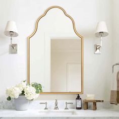 a bathroom sink with a large mirror above it and flowers in a vase on the counter